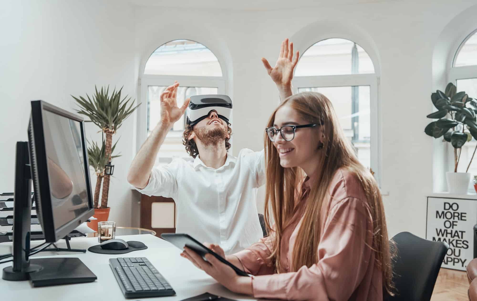 Playful office worker with virtual reality glasses and woman with tablet